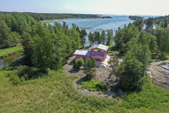 Rakennus erottuu vaaleanpunaisena väriläiskänä saaristolaismiljöössä.