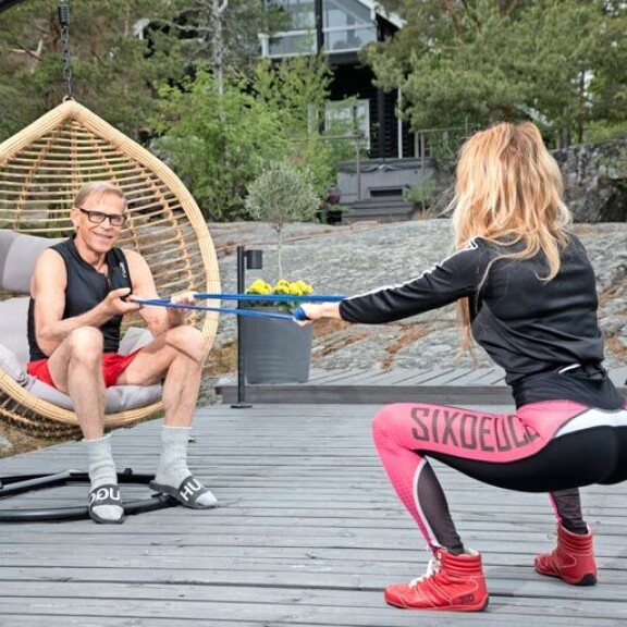 Kyykky vastuskuminauhalla korvaa puuttuvan kuntosalin. Topi kannustaa rakastaan treenaamaan myös mökillä. Kyykky vastuskuminauhalla korvaa puuttuvan kuntosalin. Topi kannustaa rakastaan treenaamaan myös mökillä.