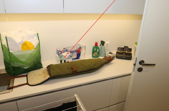 Poliisin ottama kuva alakerran kodinhoitohuoneesta. Pöydällä näkyy haulikon suojapussi sekä kaksi samanlaista patruunaa kuin aseen piipuissa olleet patruunan hylsyt.