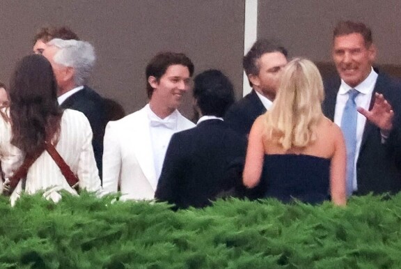 Patrick Schwarzenegger hymyili tyytyväisenä valkoisessa asussaan.