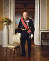Univormuun pukeutunut kuningas Harald nojaa tuoliin.
