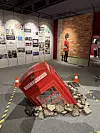 Submerged Phone Booth -teos 'uppoaa' lattiaan keskellä näyttelytilaa.