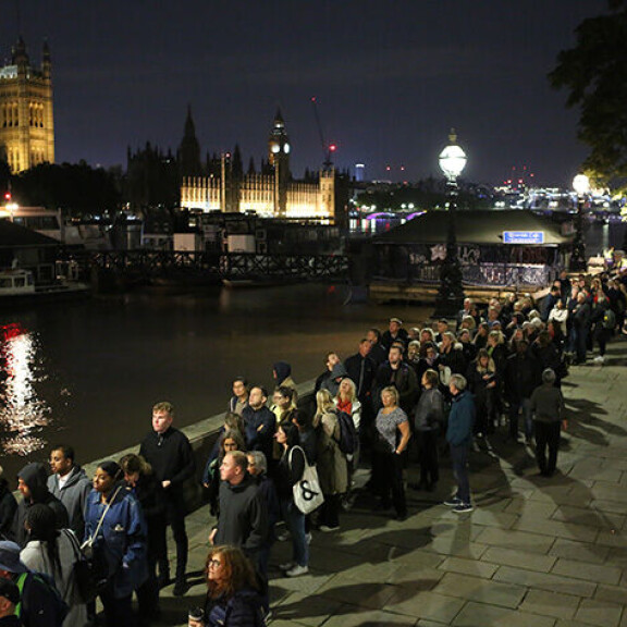 Öinen Westminsterin palatsi luo valoa Thames-joen pintaan, kun surevat kansalaiset odottavat jonon etenevän. Jono Lontoossa