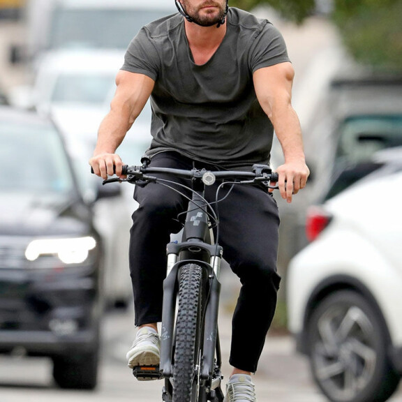 Näyttelijän lihakset pullistuivat esiin kireästä t-paidasta. chris hemsworth pyöräilevät