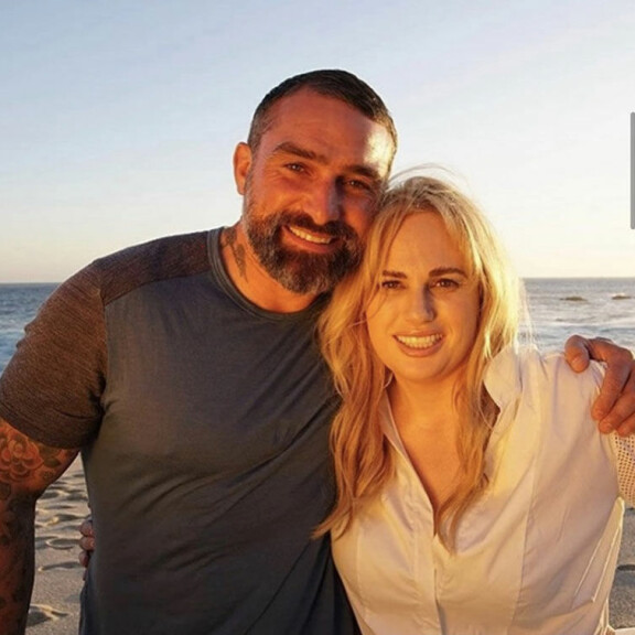 Ant ja Rebel hymyilemässä hiekkarannalla auringonlaskussa. Rebel ja ant