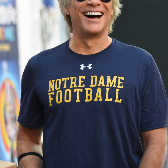 Nauravan rokkarin käsivarressa roikkui musta kasvomaski. jon bon jovi nauraa